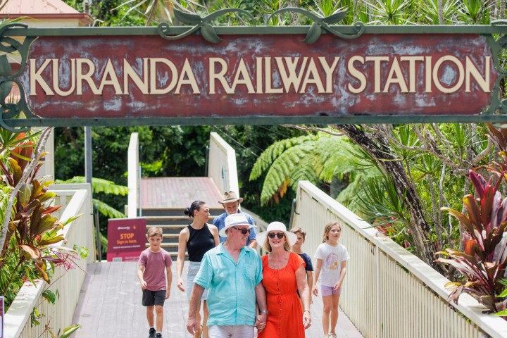 a group of people walking on a sidewalk near a fence