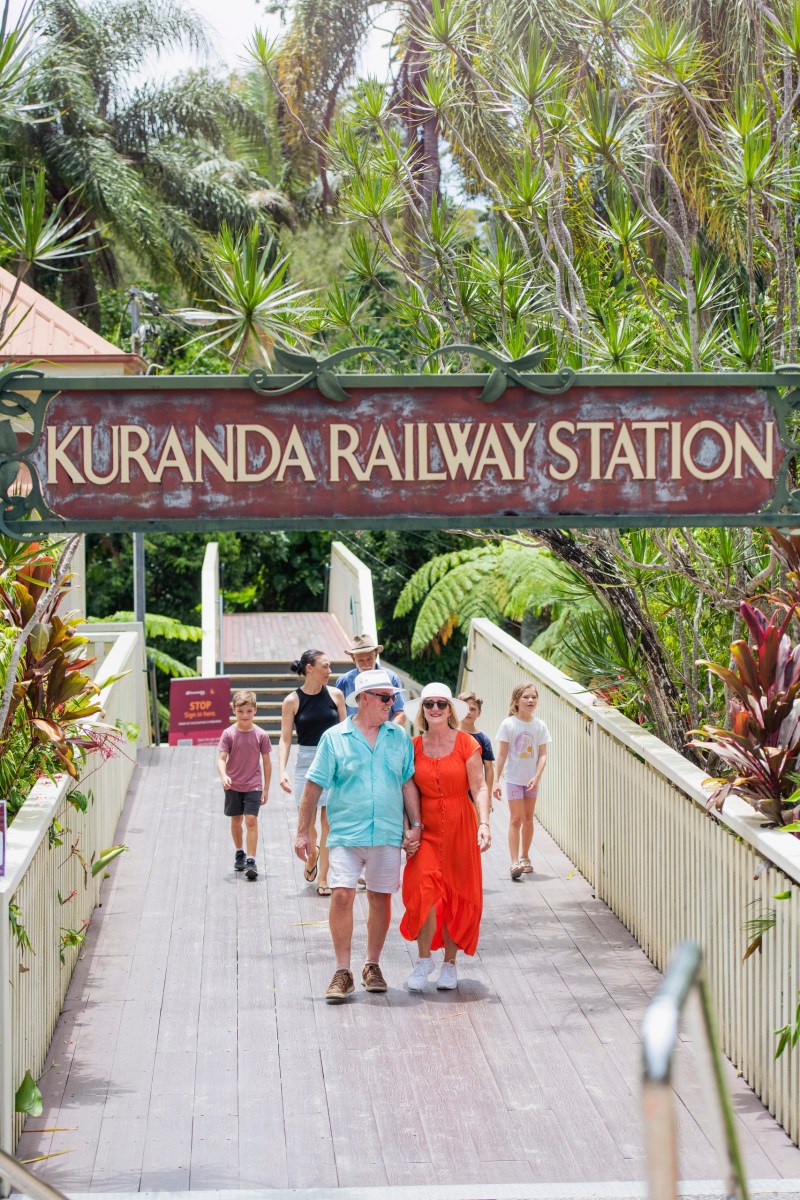 a group of people walking on a sidewalk near a fence
