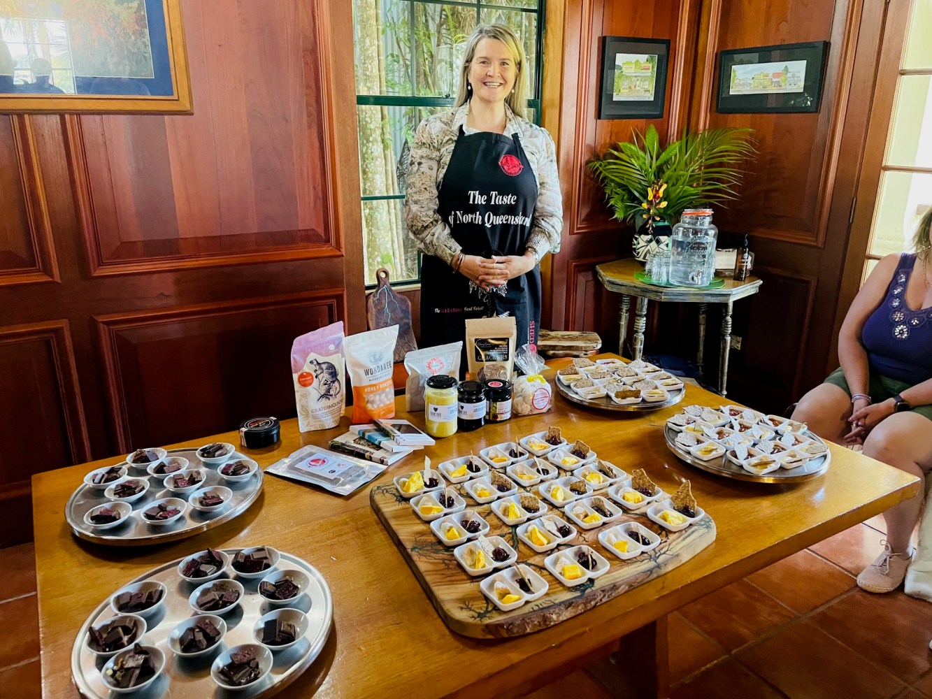 Woman in apron stands by table with chocolates and product samples.