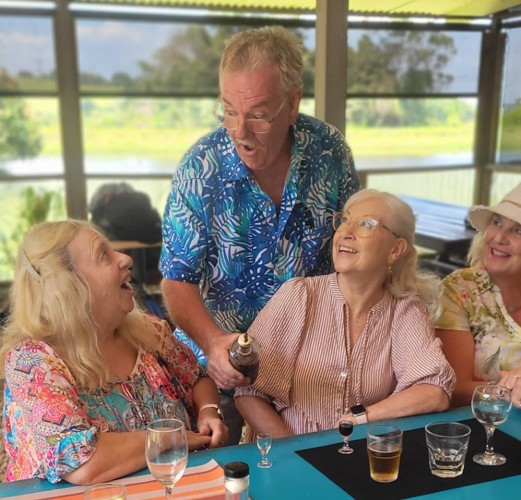 Three women and a man laughing at a table outdoors with drinks