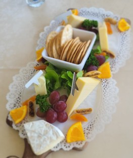 Cheese platter with crackers, grapes, figs, and orange slices on a decorative doily.