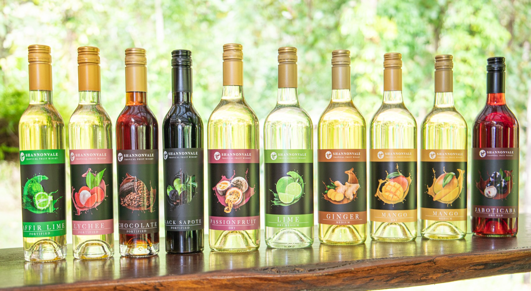 Ten bottles of fruit wine with colorful labels on a wooden surface.