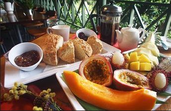 Tropical breakfast with fruits, pastries, jam, and coffee on a balcony.