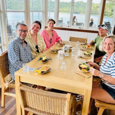 Six people dining at a wooden table with a scenic window view of a lake and trees.