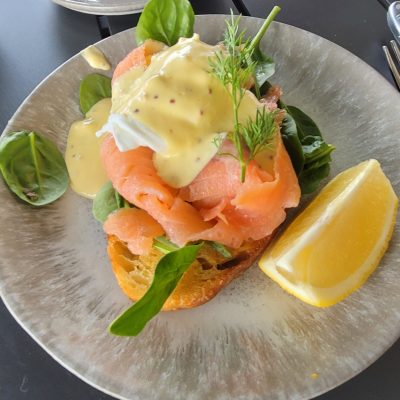 Plate with smoked salmon, poached egg, spinach, and hollandaise, with a lemon wedge; cup and saucer nearby.