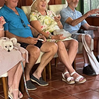 Three seated people smiling with a small white dog on a leash indoors.