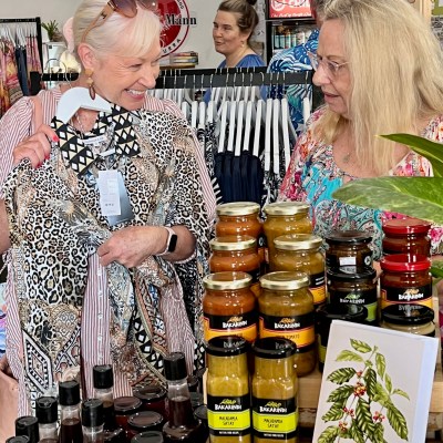 Two women smiling while shopping in a store selling clothing and jars of condiments.