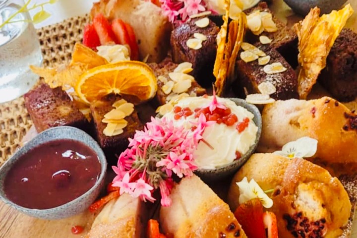 Assorted desserts with flowers, fruit, and sauces on a wooden board.